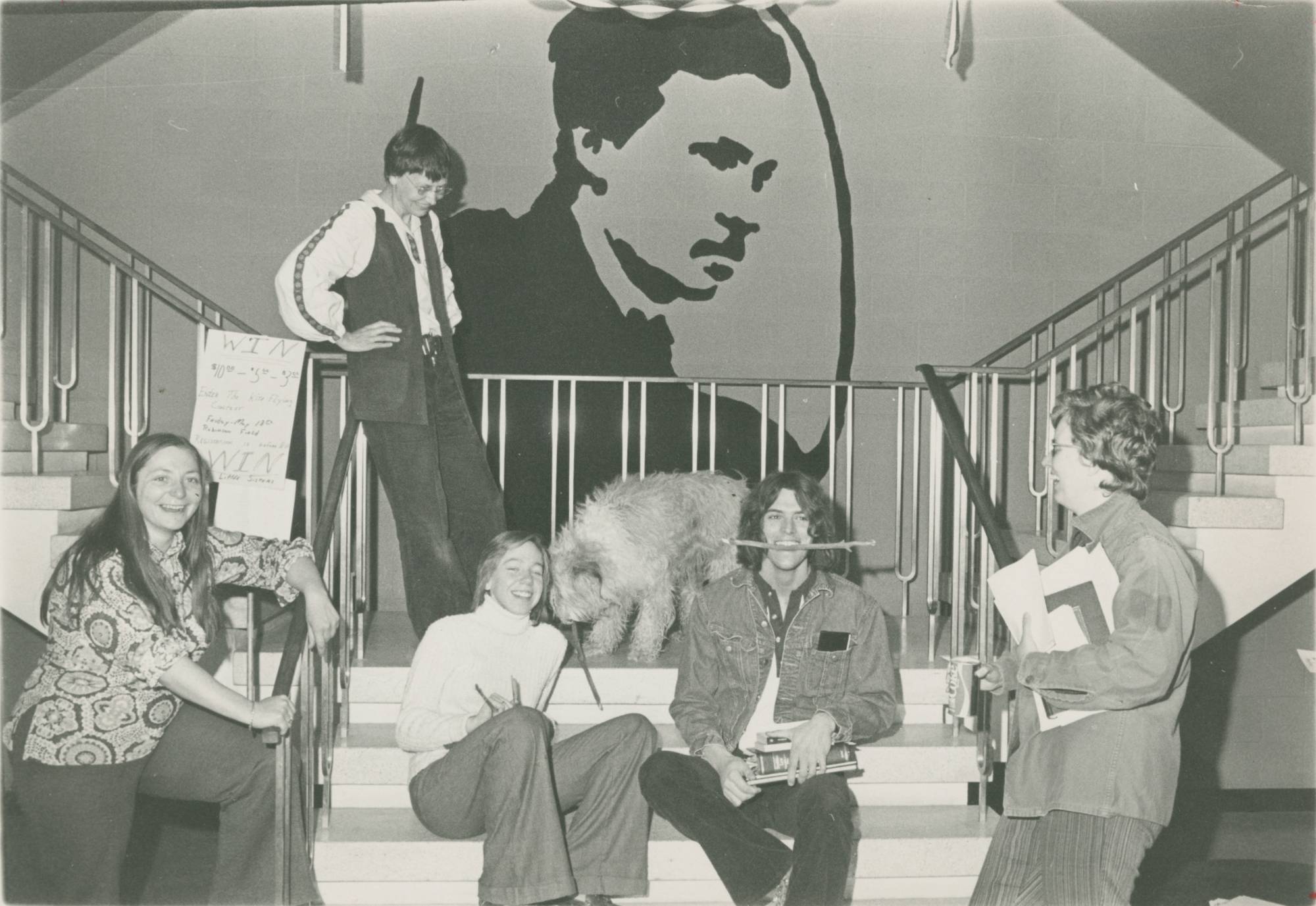 A black and white photo of students and faculty sitting and standing on the stairs in front of the William James mural in Lake Superior Hall.